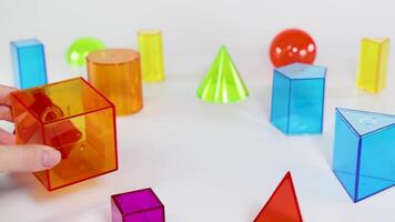 Hands interact with colorful 3D shapes on a white surface, demonstrating basic geometry concepts in a playful setting video