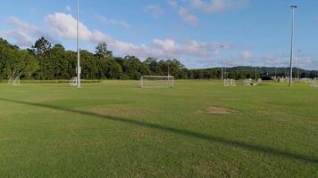 Aerial footage captures an empty soccer field under clear skies, showcasing goalposts and lush greenery in the background video