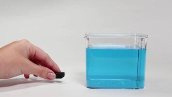 A hand places a rubber foam block in water, demonstrating buoyancy. Clear lighting and simple composition highlight the scientific process video