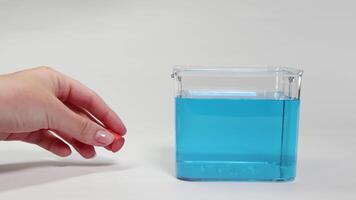 A hand drops a red object into a clear container with blue liquid, observing its sinking behavior video