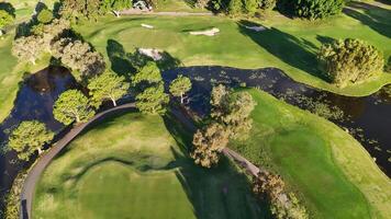 Drone footage captures a lush golf course with fairways, bunkers, and water hazards under bright sunlight video