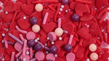 Vibrant candy sprinkles cascade onto a base of red heart-shaped candies, creating a lively and colorful composition video