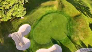 Drone captures a golf course with bunkers and green under golden hour lighting, highlighting shadows and landscape contours video