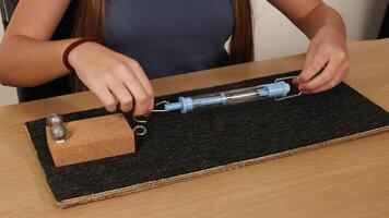 A person conducts a friction experiment using a spring scale, weights, and a textured surface on a table video