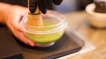 Hands whisk matcha in a bowl with precision. Soft lighting enhances the serene atmosphere of this traditional tea-making process video