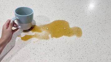 A hand accidentally spills coffee from a mug onto a kitchen countertop, creating a mess in bright lighting video
