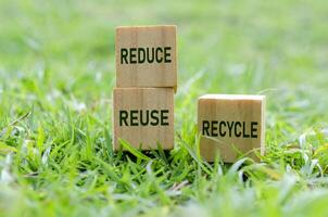 Wooden cubes labeled REDUCE, REUSE and RECYCLE on grass. Promoting sustainability. photo