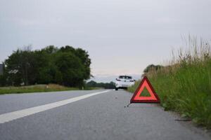 A warning triangle, behind it a white car with a breakdown photo