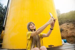 Woman Taking a Selfie in Front of a Bright Yellow Tank in a Natural Setting photo