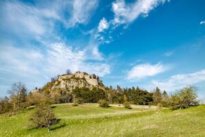 Bottom view of a hill with the ruins of the Hohentwil castle on its top against a blue skyHill with Hohentwil castle ruins against sky photo