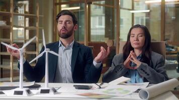 Multiethnic relaxed business team meditating wind turbine startup windmill models eco engineers Korean woman Caucasian man stress relief sustainable energy green focus harmony innovation peaceful rest video