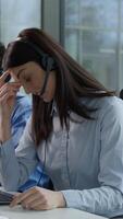 Tired exhausted Caucasian business woman callcenter worker headset touch head suffer headache pain burnout working computer online sales trading helpline multiethnic coworkers work problem call center video