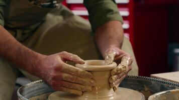 Joyful laughing Caucasian male man guy potter ceramist craftsman small business owner working with clay brown material spinning wheel pottery looking at camera smile wide indoors workshop art studio video