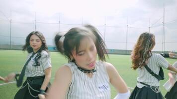 A lively scene featuring a group of young dancers performing on a grassy field. The focus is on a girl in the foreground with playful pigtails, wearing a striped outfit. video
