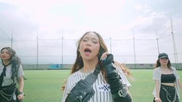 A group of dancers performing on a sports field, wearing stylish outfits with stripes. The lead dancer poses confidently in the foreground, showcasing a vibrant and energetic atmosphere. video