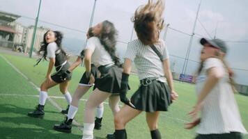 Three dancers performing energetically on a sports field, showcasing dynamic movements and stylish outfits. The background features a cityscape under a cloudy sky. video