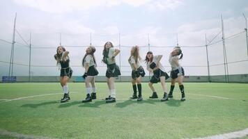A group of six dancers performing a choreographed routine on a green field under a bright sky. They are dressed in stylish outfits, showcasing dynamic poses and expressions. video