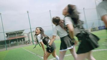 A dynamic scene of a group of young women dancing on a sports field, wearing stylish outfits. The background features a sports facility and a cloudy sky, creating an energetic atmosphere.H video