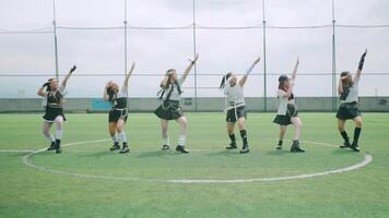 A group of six female dancers performing a choreographed routine on a sports field. They wear matching outfits with a sporty vibe, showcasing dynamic movements and expressions video