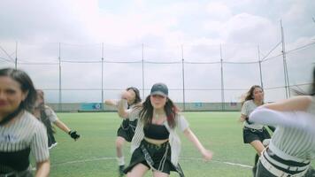A group of four dancers performing on a green field under a cloudy sky. They wear stylish outfits and are in motion, showcasing their dance skills. video