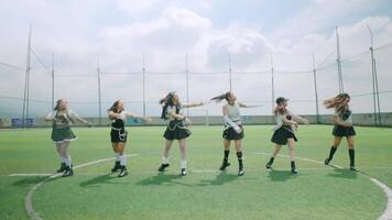 A group of six dancers performing on a sports field under a bright sky. They are dressed in stylish outfits, striking dynamic poses, showcasing their choreography. video