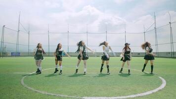 A group of six dancers performing on a grassy field under a cloudy sky. They wear stylish outfits, showcasing energetic dance moves. The scene captures a vibrant and dynamic atmosphere. video