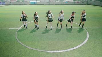 A group of six young women performing a dance routine on a soccer field. They are dressed in matching outfits, showcasing energetic movements and smiles. video