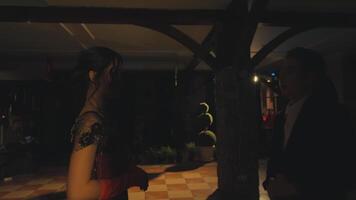 A couple dancing at a festive event, with one person in a colorful dress and the other in a suit. The setting is illuminated with soft lights, creating a romantic atmosphere. video