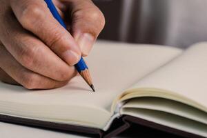 Close up image of pencil in people's hand start writing down something in the empty open book for study, learning, idea concept. photo