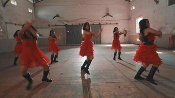 A group of dancers in red dresses performing a choreographed routine in an empty warehouse. The dancers are in various poses, showcasing movement and energy. video