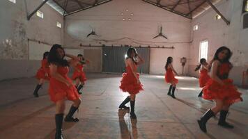A group of dancers in red dresses performing in an industrial space. The dancers are in various poses, showcasing energy and movement. The venue has a rustic feel with high ceilings and wooden floors. video