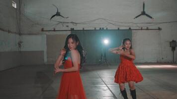 Two young women in red dresses dancing in an industrial space with dim lighting and a spotlight. video