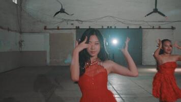 Three women in red dresses performing a dance routine in an industrial space. The central dancer poses gracefully, while the others mirror her movements. Soft lighting enhances the scene. video