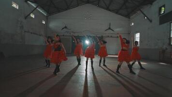 A group of dancers in red dresses performing in an industrial space with high ceilings and minimal lighting. The focus is on their synchronized movements and expressions. video