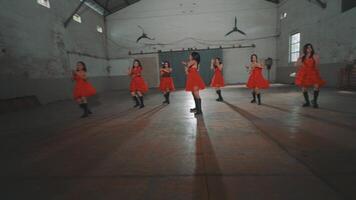A group of dancers in red dresses performing in an industrial space with high ceilings and wooden floors. The atmosphere is energetic and dynamic, showcasing their synchronized movements. video