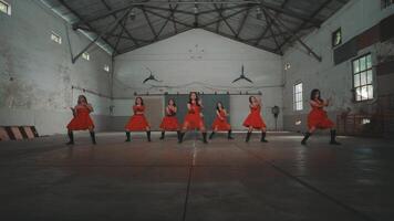A group of dancers in red dresses performing in an industrial space with high ceilings and large windows. The atmosphere is energetic and dynamic, showcasing their synchronized movements. video