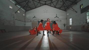 A group of dancers in red dresses performing in an industrial space with high ceilings and large windows. The energetic choreography showcases their synchronized movements. video
