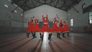 A group of six dancers in red dresses performing in an industrial space with high ceilings and shadows on the floor. video
