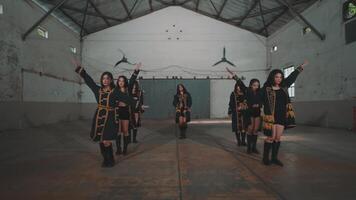 A group of dancers performing a synchronized routine in an industrial space with high ceilings and minimal decor. The dancers are in a dynamic pose, showcasing their skills and teamwork. video