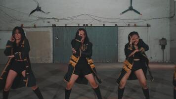 A dynamic dance scene featuring performers with flowing hair, captured in motion. The background shows an industrial setting with a large metal door and overhead fans. video