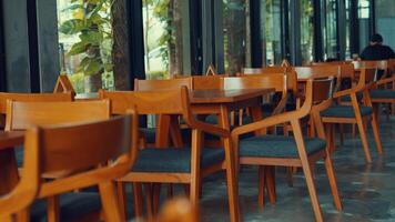 A cozy cafe interior featuring wooden tables and chairs arranged neatly. The space is well-lit with large windows allowing natural light to flood in, creating a warm atmosphere video