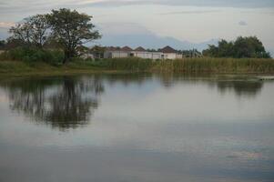 Lake reflects trees and distant houses under a soft sky photo