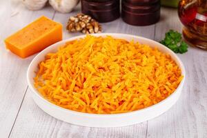 A bowl of shredded cheese on a table next to a bottle of butter photo