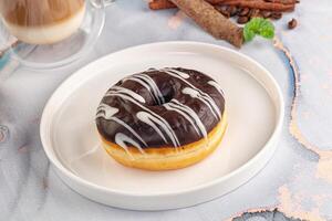 A chocolate glazed doughnut on a white plate with cinnamon and coffee photo