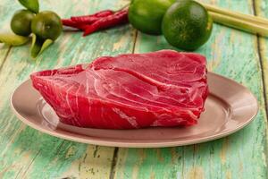 A piece of raw meat on a plate with lime and green peppers photo