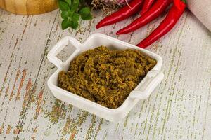 A bowl of green curry paste with red peppers and other spices photo