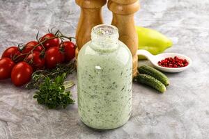 A bottle of dressing sitting next to a pepper and a tomato photo