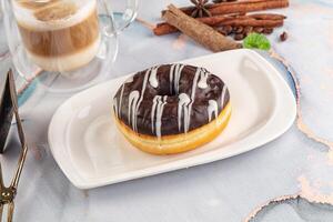 A donut on a plate with a cup of coffee and cinnamon sticks photo