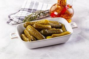 Pickles in a white dish with a bottle of vinegar and a sprig of rosemary photo