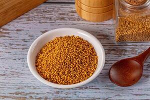 Mustard seeds in a bowl and wooden spoon on a wooden table photo